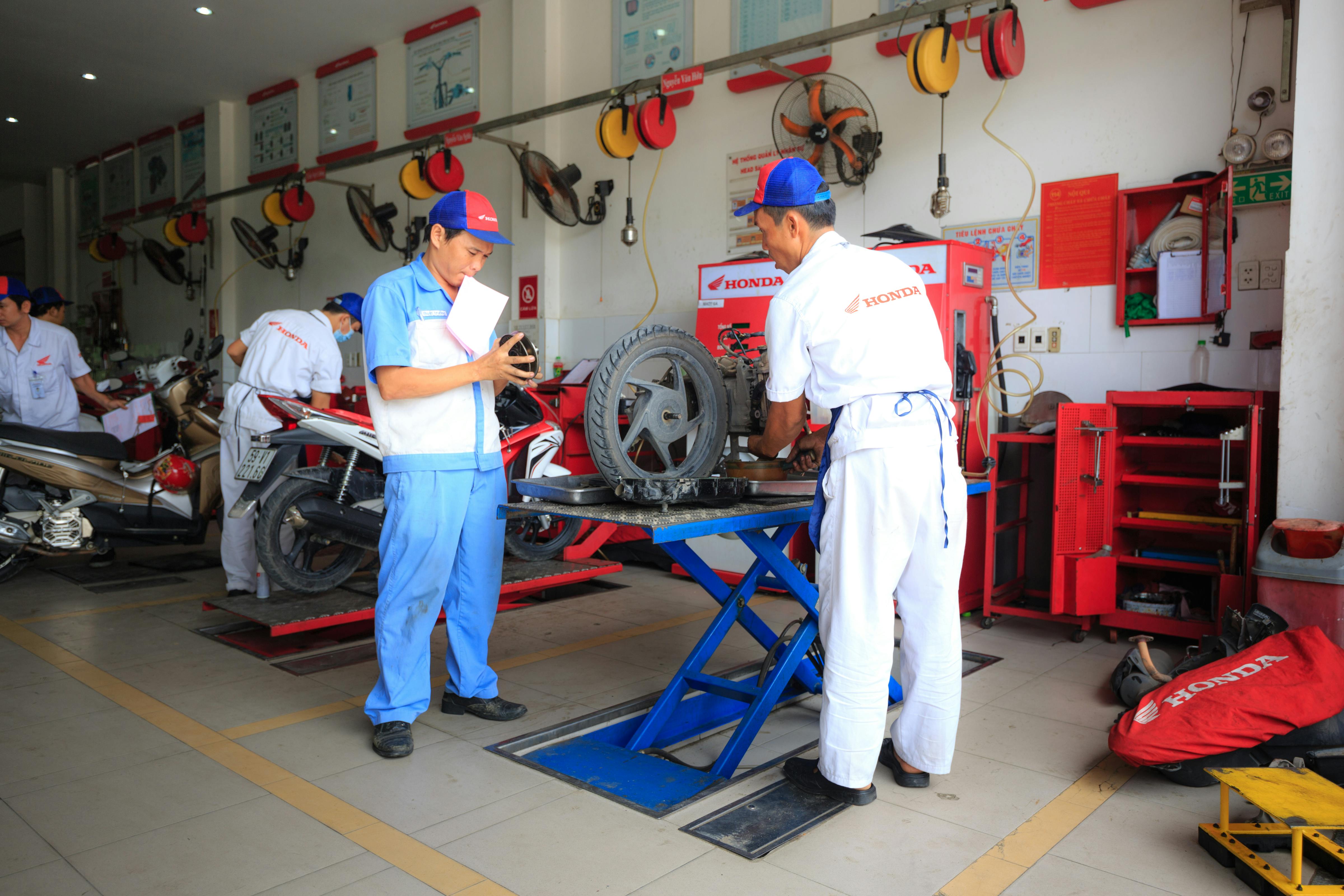 Mechanics wearing uniforms work on motorcycles inside a Honda service center.