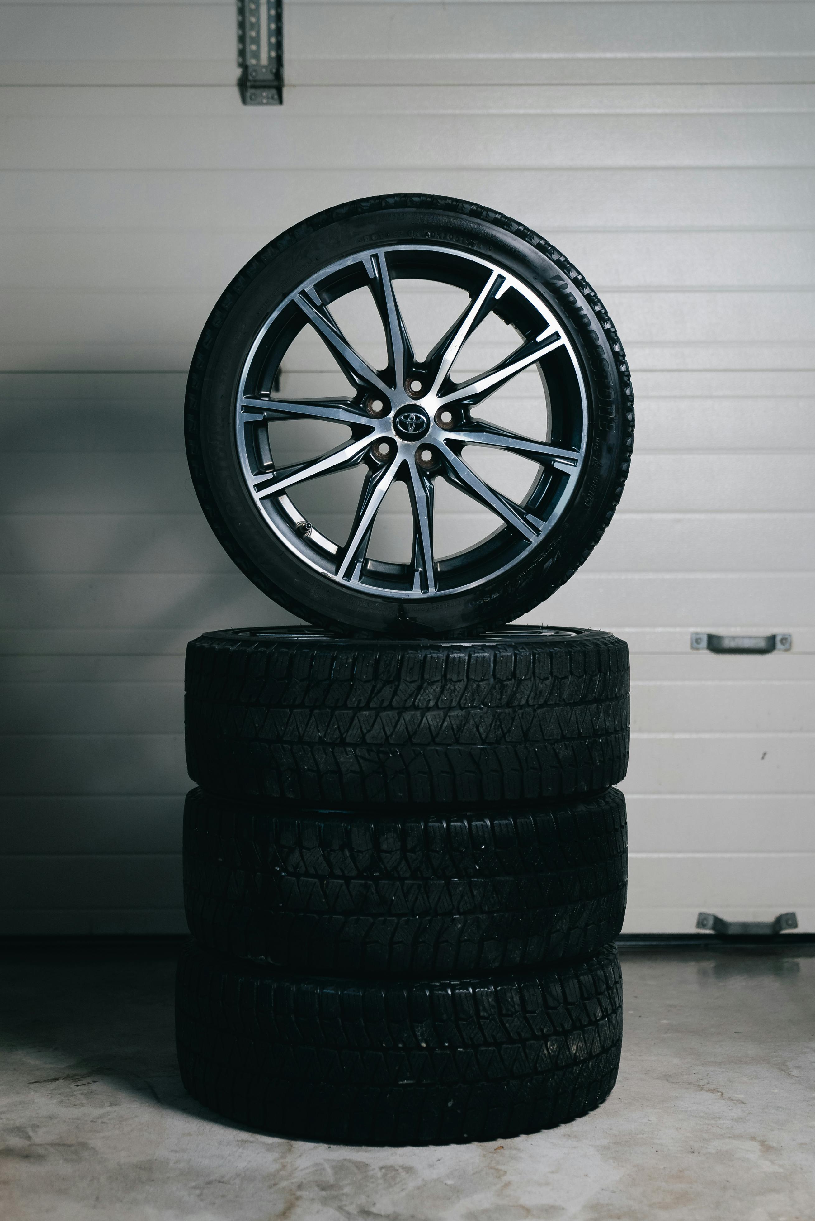 Car tires stacked with an alloy wheel on top in a garage setting. Perfect for automotive themes.